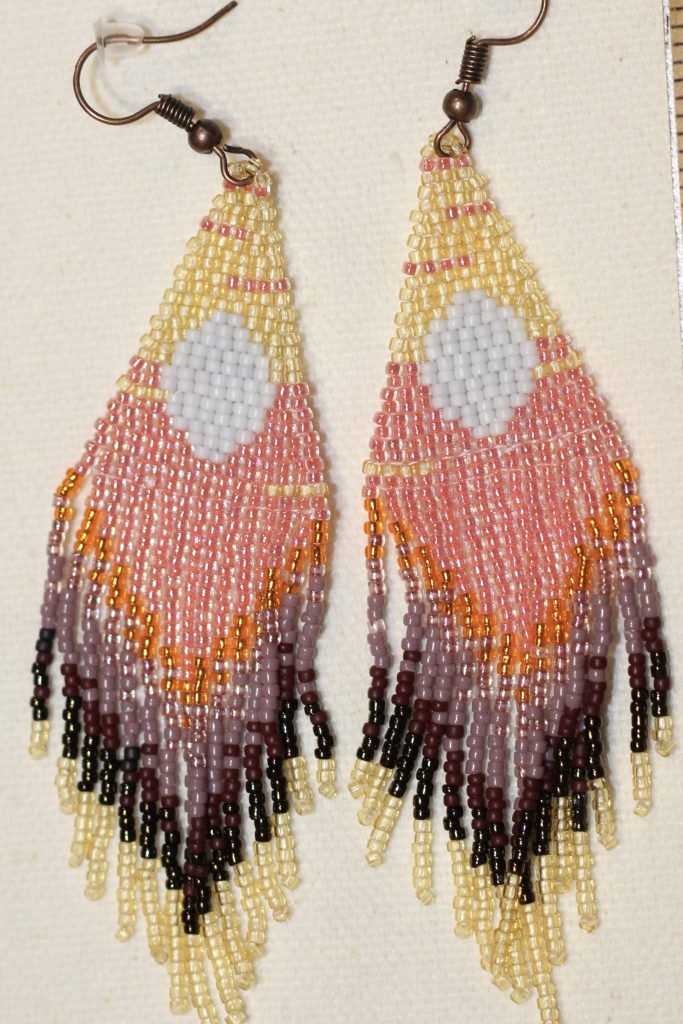 "Capture the beauty of sunrise with these handmade earrings, showcasing soft transparent yellow, coral, bright orange, shiny purple, and matte purple, all centered around a white circle. The design is finished with an elegant black accent. Crafted with 15/0 seed beads in the brick stitch, these earrings are perfect for anyone who loves unique, colorful accessories. Measurements: 0.80 inches wide, 3.75 inches long."