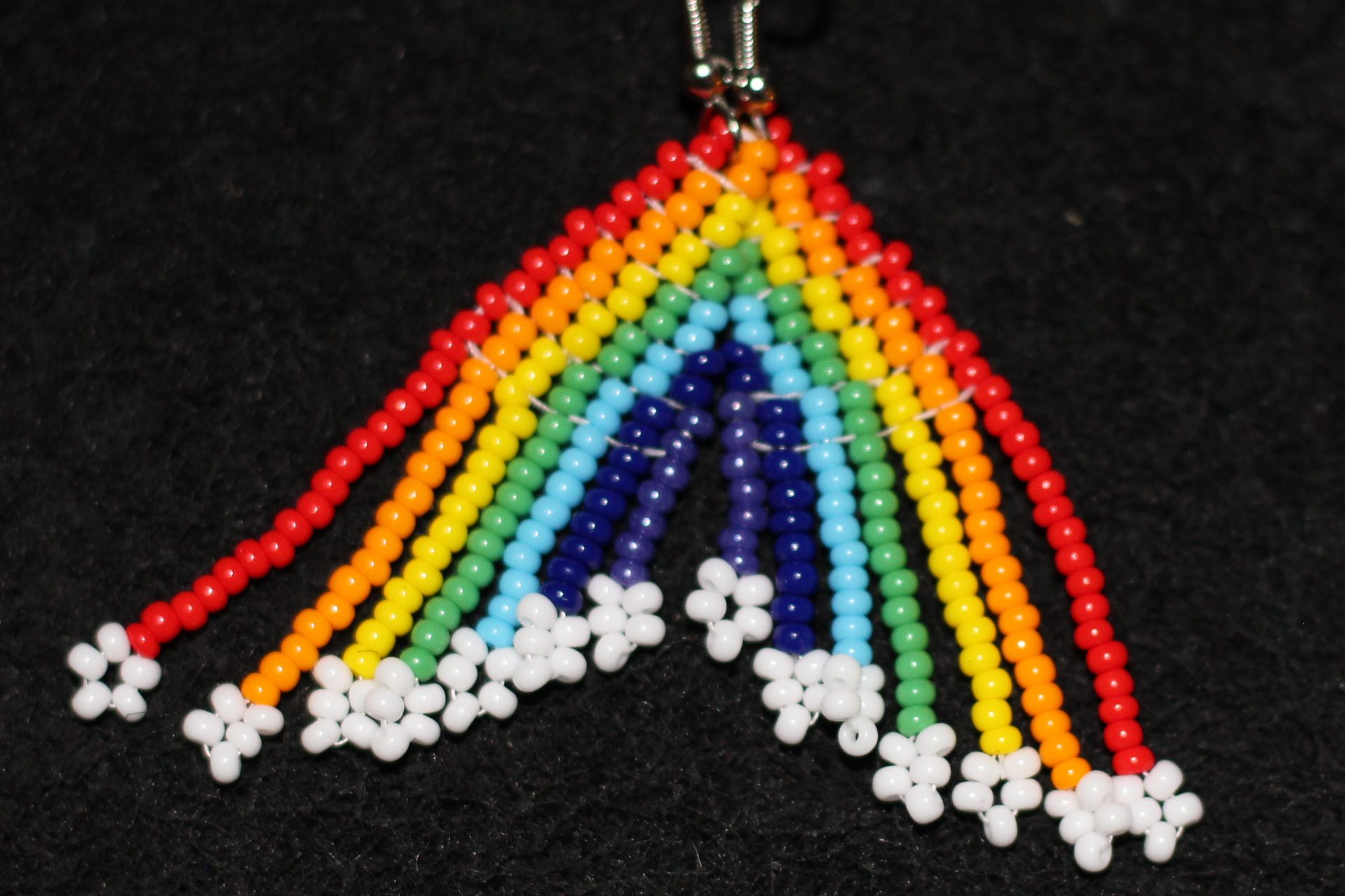 "Bring the rainbow to your ears with these playful handmade earrings! Both earrings together form a complete rainbow with soft diagonal sloped fringe ending in white cloud-like beads. Crafted with 11/0 seed beads in the brick stitch, these earrings are a cheerful and creative addition to your accessory collection. Measurements: 0.55 inch wide, 2.60 inches long."
